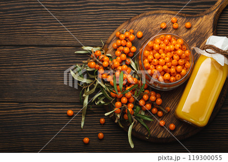 Sea buckthorn healthy drink in bottle, ripe berries in glass jar and branches with leaves top view on dark wooden rustic background, great for skin, heart, vessels and immune system. Copy space. Sea buckthorn healthy drink in bottle, ripe berries in glass jar and branches with leaves top view on dark wooden rustic background, great for skin, heart, vessels and immune system. Copy space. 119300055