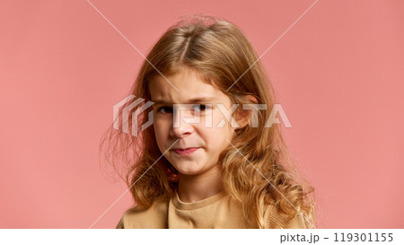 Girl with curly hair, frowns slightly, lips pressed together, showing discomfort or suspicion. against soft pink studio background. Girl with curly hair, frowns slightly, lips pressed together, showing discomfort or suspicion. against soft pink studio background. 119301155