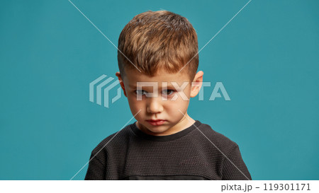 Little boy stares intently with a serious, determined expression against blue studio background. Little boy stares intently with a serious, determined expression against blue studio background. 119301171
