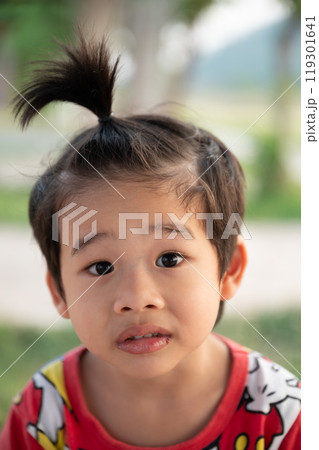 Young child with a playful hairstyle outdoors in a green natural setting on a sunny day enjoying childhood moments 119301641