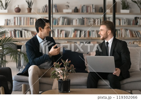 Positive successful young male business colleagues talking in lobby space 119302066