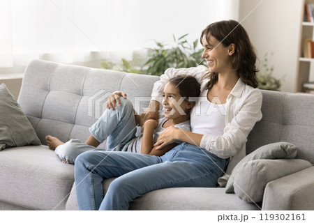 Serene young mother sitting on sofa embracing child daughter dreaming 119302161