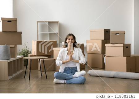 Happy young lady meditate on floor moving in new apartment Happy young lady meditate on floor moving in new apartment 119302163