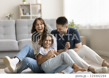 Laughing millennial spouses with preteen daughter playing tickling on floor 119302284