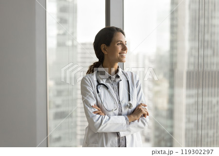 Happy young lady physician stand by window look at distance 119302297