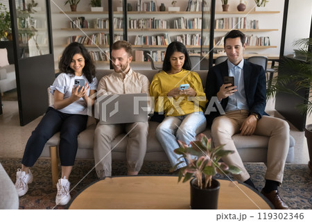 Focused diverse team of gadget addicted users sitting on sofa 119302346