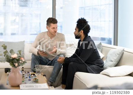 Two multiethnic business colleagues discussing work tasks on office couch 119302380