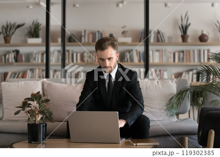 Serious young businessman in suit and tie working at laptop Serious young businessman in suit and tie working at laptop 119302385