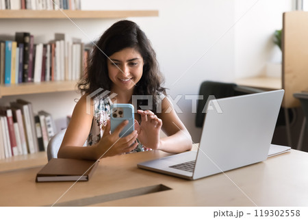 Positive young Indian businesswoman in casual using smartphone Positive young Indian businesswoman in casual using smartphone 119302558