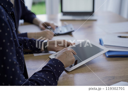 Accountants or auditors reviewing financial documents while sitting at the wooden desk in office. Professionals are analyzing paper reports using tablet computer, close up. Audit and taxes 119302701