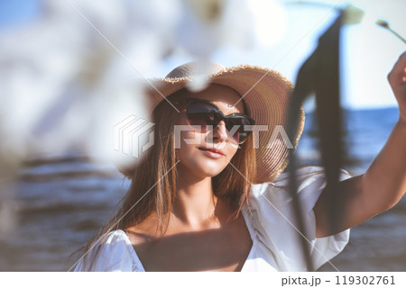 Happy smiling woman is on ocean beach. View through white blurred flowers Happy smiling woman is on ocean beach. View through white blurred flowers 119302761