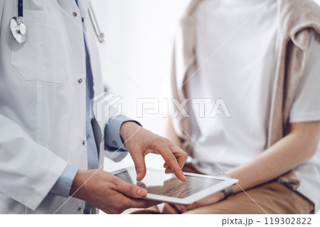 Doctor and patient in clinic. Friendly physician using tablet computer near a young woman. Medicine concept 119302822