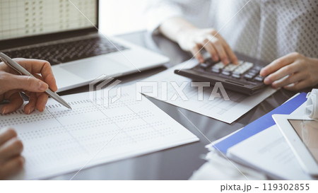 Woman accountant using a calculator and laptop computer while counting taxes for a client. Business audit concepts 119302855