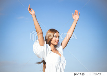 Happy, beautiful woman on the ocean beach standing in a white summer dress, raising hands Happy, beautiful woman on the ocean beach standing in a white summer dress, raising hands 119302936