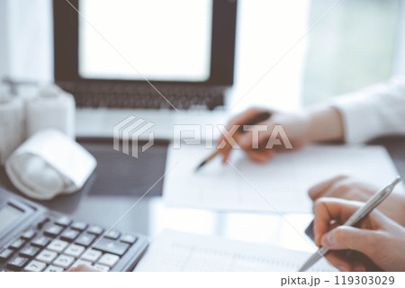 Two accountants use a calculator and laptop computer for counting taxes or revenue balance. Business, audit, and taxes concepts Two accountants use a calculator and laptop computer for counting taxes or revenue balance. Business, audit, and taxes concepts 119303029
