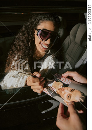 Vertical shot of smiling successful Middle Eastern female singer sitting in car signing photo 119303316