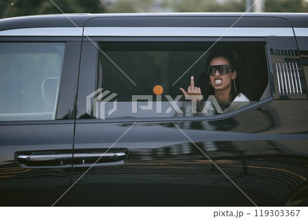 Shot through open car window of pissed off Middle Eastern female celebrity showing middle finger to paparazzi while wearing trendy sunglasses sitting in backseat of limo, copy space 119303367