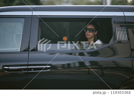 Shot through open car window of successful Middle Eastern woman in trendy sunglasses sitting in back seat of limo embodying celebrity lifestyle while arriving at award ceremony, copy space 119303368