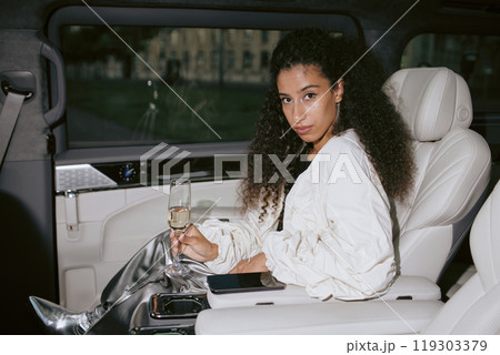 Young glamorous Middle Eastern woman smiling in back seat of car holding glass of champagne as birthday celebration, camera flash, copy space Young glamorous Middle Eastern woman smiling in back seat of car holding glass of champagne as birthday celebration, camera flash, copy space 119303379