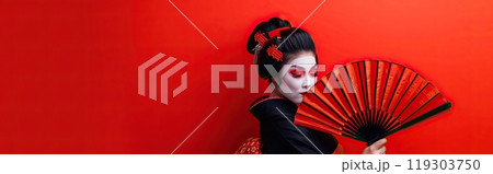 In front of a red background, a geisha is holding an umbrella 119303750