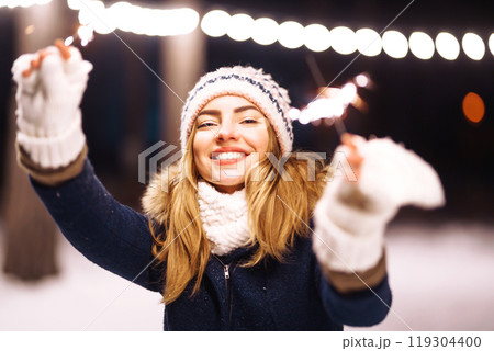 Cheerful young woman holding a sparkler in hand in forest. Woman happiness and playing firework. 119304400