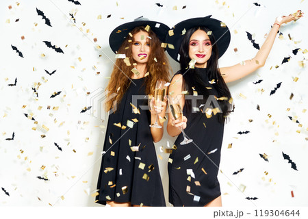 portrait of two happy young women in black witch halloween costumes. firecrackers in the background. 119304644