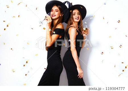 nice portrait of two beautiful young woman in black witch halloween costumes on party over white background. nice portrait of two beautiful young woman in black witch halloween costumes on party over white background. 119304777