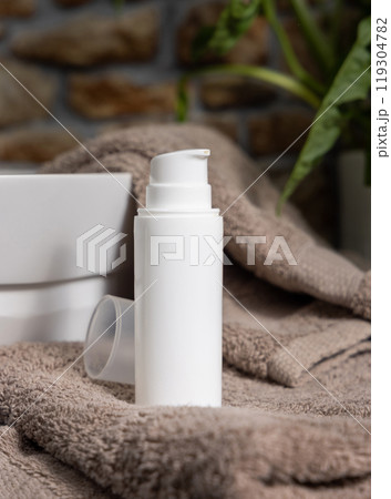 White cosmetic pump bottle on brown towels near basin and green plant close up, mockup 119304782