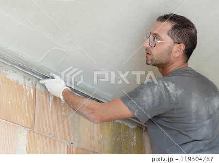 Craftsman in dirty gloves and gray shirt checking the ceiling surface with straight edge Craftsman in dirty gloves and gray shirt checking the ceiling surface with straight edge 119304787