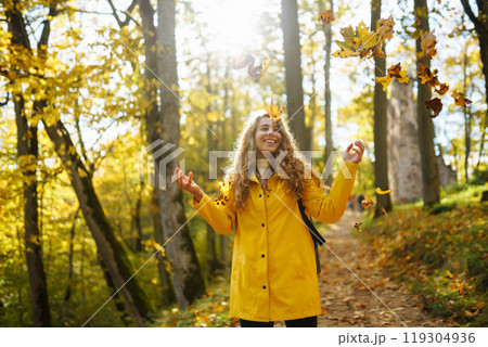 Woman in a yellow coat with backpack walks along wooden staircase, enjoying autumn scenery in forest 119304936