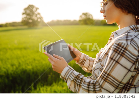 A woman farmer with modern tablet evaluates the shoots with her hand. Farm work with digital tablet. A woman farmer with modern tablet evaluates the shoots with her hand. Farm work with digital tablet. 119305542