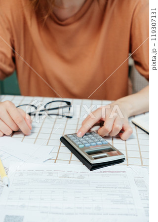 close-up woman's hands pays bills online, sits in kitchen receipts and calculator. close-up woman's hands pays bills online, sits in kitchen receipts and calculator. 119307131