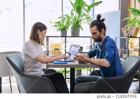 Young man woman sitting at table in coworking space with laptop smartphone, talking together 119307359