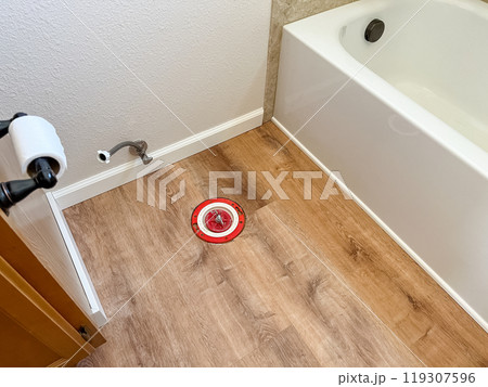 A bathroom under renovation featuring new vinyl flooring and a removed toilet. The base plumbing and toilet paper holder remain, while the area is prepared for the next installation step. 119307596