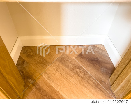 White vinyl baseboards and trim pieces are neatly stacked against a wall, prepared for installation in a room with wooden flooring. The renovation project is in progress, ready to complete the room 119307647