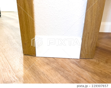 White vinyl baseboards and trim pieces are neatly stacked against a wall, prepared for installation in a room with wooden flooring. The renovation project is in progress, ready to complete the room White vinyl baseboards and trim pieces are neatly stacked against a wall, prepared for installation in a room with wooden flooring. The renovation project is in progress, ready to complete the room 119307657