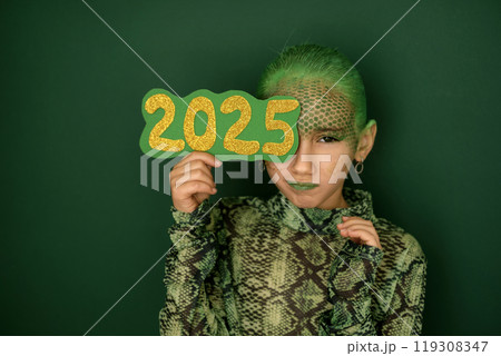 A girl with a dissatisfied face, disguised as a snake, covers face with the number 2025. The symbol of the new year according to the Eastern calendar A girl with a dissatisfied face, disguised as a snake, covers face with the number 2025. The symbol of the new year according to the Eastern calendar 119308347