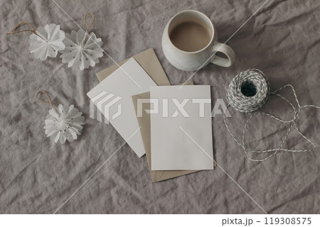 Winter festive still life. Handmade Christmas ornaments, decoration. White paper snowflakes on beige linen tablecloth. Cup of coffee. Blank greeting cards, invitations mockup. Festive flat lay, top Winter festive still life. Handmade Christmas ornaments, decoration. White paper snowflakes on beige linen tablecloth. Cup of coffee. Blank greeting cards, invitations mockup. Festive flat lay, top 119308575
