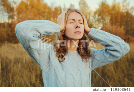 Upset exhausted young woman with headache, pain tension in the head, suffers from migraine outdoors 119308641