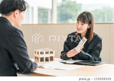 住宅模型や設計図を使って顧客にマイホームの説明・商談をするビジネスウーマン 119309320