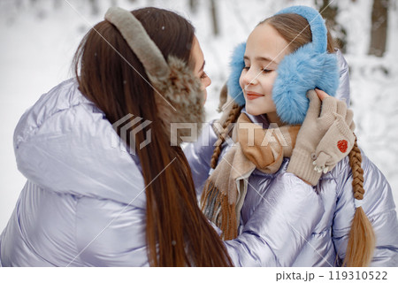 Mother with her child having fun in forest on winter day. Girls wearing purple warm jackets and earmuffs. Female models posing for a photo. Mother with her child having fun in forest on winter day. Girls wearing purple warm jackets and earmuffs. Female models posing for a photo. 119310522