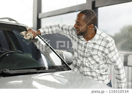 Man washing luxury car on a car wash with a rag. Black man wiping his car. Man wearing plaid shirt, smiling. Man washing luxury car on a car wash with a rag. Black man wiping his car. Man wearing plaid shirt, smiling. 119310534