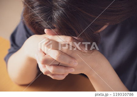 両手を組んでうつむく中年女性 119310786