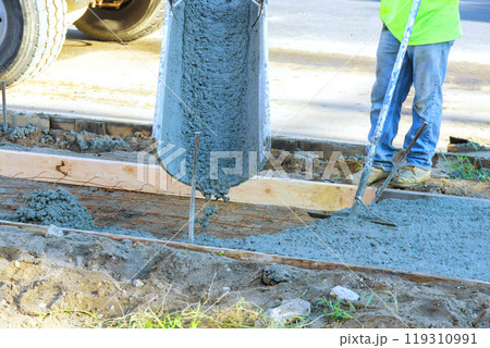Concrete mixer truck is pouring fresh concrete onto reinforced bars for new sidewalk 119310991