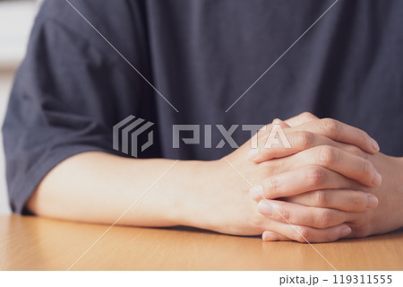 机の上で両手を組む中年女性の手元 119311555
