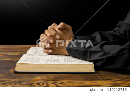 Man praying with his hands on a opened holy bible on wooden table. Symbol of faith and worship in God. People christianity prayer in church Man praying with his hands on a opened holy bible on wooden table. Symbol of faith and worship in God. People christianity prayer in church 119312716