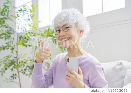 スマートフォンを持ってグッドサインするシニア女性　リビングルーム 119313031