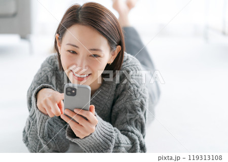 床に寝転びスマホを操作する女性 119313108