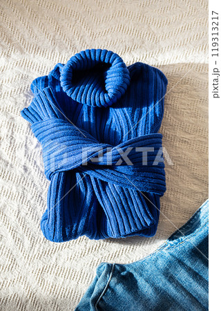 Trendy warm sweater with high collars and blue jeans on bed. Autumnal outfit. Trendy warm sweater with high collars and blue jeans on bed. Autumnal outfit. 119313217