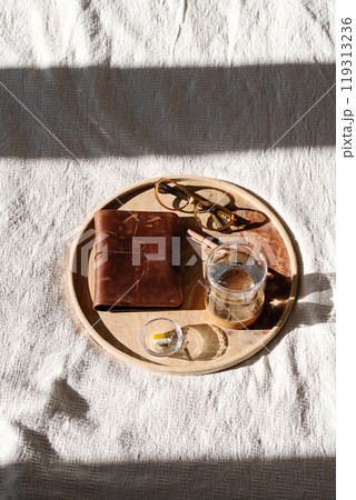 Wooden tray displaying vitamin dose, glass of water, notebook and glasses. Morning routine concepts. Wooden tray displaying vitamin dose, glass of water, notebook and glasses. Morning routine concepts. 119313236